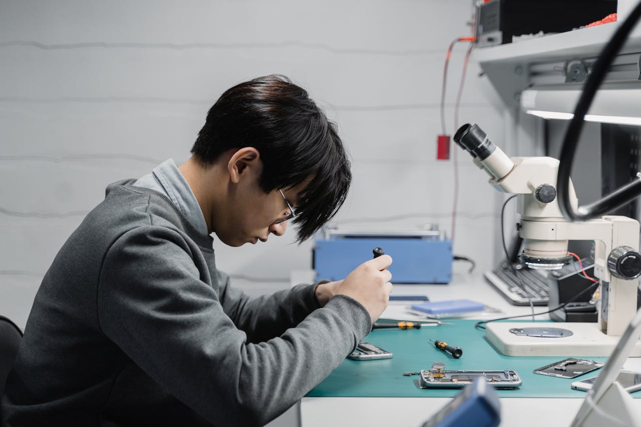 about-us Professional technician repairing mobile devices using a microscope in a lab.